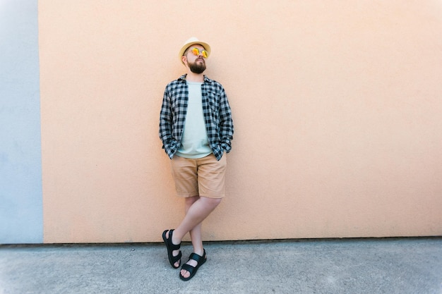 Bearded man in summer clothes and hat stand over beige wall on street city urban and travel concept copy space and empty space for advertising