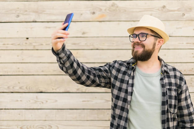 Bearded man takes selfie with smartphone during summer city break over wooden wall selfie photos and social media app concept