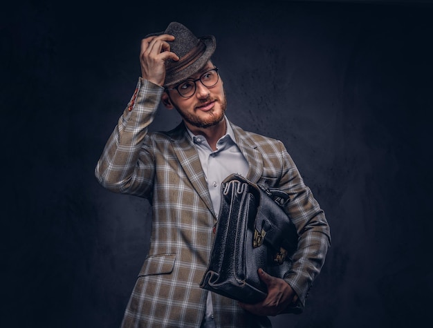 A bearded man wearing casual suit in a hat and glasses holds sui