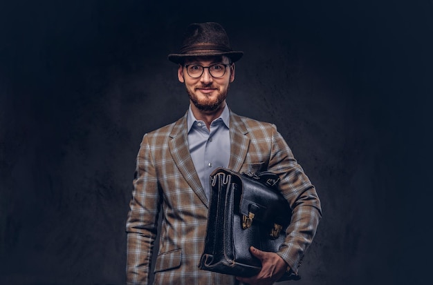 A bearded man wearing casual suit in a hat and glasses holds sui