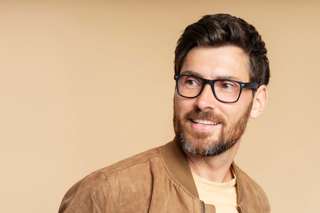 bearded man wearing stylish eyeglasses looking away isolated on beige background copy space