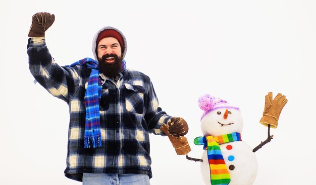 Bearded man in winter clothes holds snowman by hand winter fashion snowman in hat scarf gloves