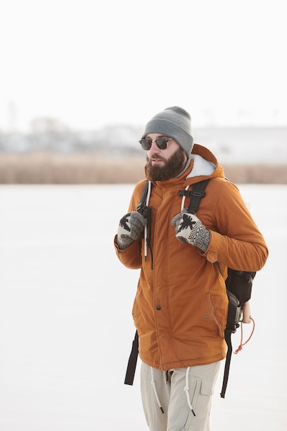 A bearded man with a backpack in warm winter clothes is walking on a frozen lake in winter The concept of hiking and active lifestyle