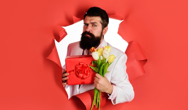 Bearded man with bouquet of flowers and gift box romantic male with present and tulips valentines