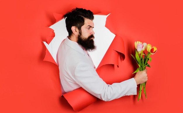 Bearded man with bouquet of flowers looking through paper hole businessman with bouquet of tulips