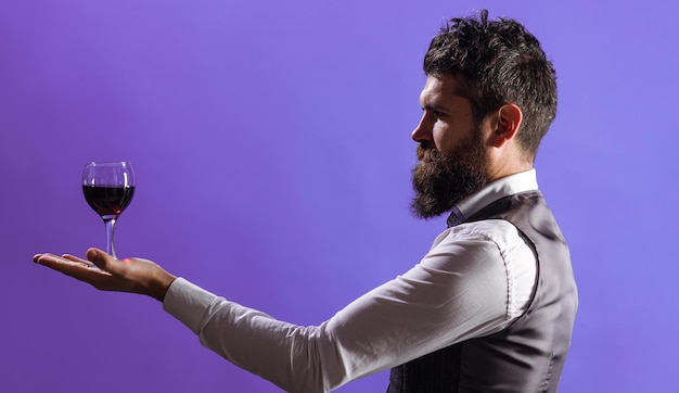 Bearded man with glass of red wine on palm hand sommelier tasting alcohol waiter in restaurant