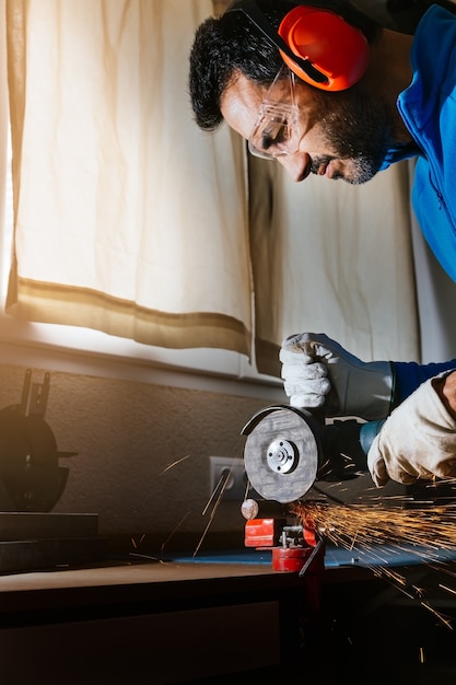 Bearded man with goggles, headphones and protective gloves cutting an iron bar with a circular saw