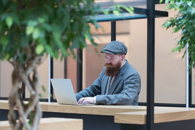 Bearded man in wool blazer working on a laptop in cafe