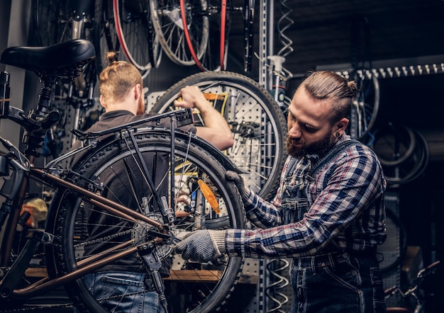 Bearded mechanic doing bicycle wheel service manual in a workshop.