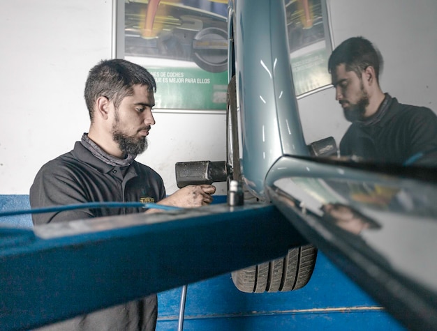 Bearded mechanic with screwdriver repairing car wheel in workshop