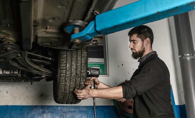 Bearded mechanic with screwdriver repairing car wheel in workshop