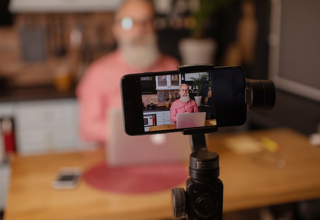 Bearded senior blogger recording video at home.