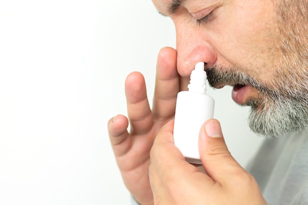 Photo bearded senior man applying spray for runny nose. treatment of colds and flu concept