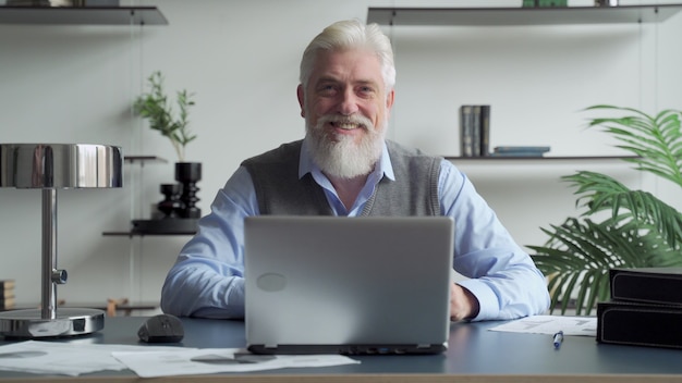 Bearded senior man working with laptop in office