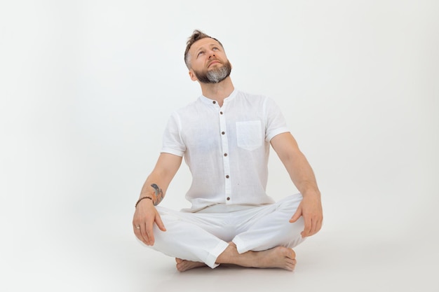 Bearded sporty handsome man tutor sit in lotus posture on white background yoga zen and eastern phil