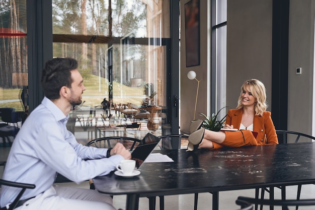 Bearded young Caucasian office worker with a laptop looking at his attractive stylish female boss