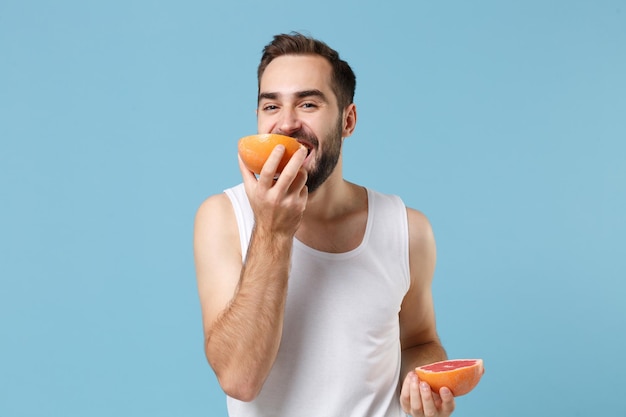 Bearded young man 20s years old in white shirt hold in hand half of grapefruit isolated on blue pastel background, studio portrait. Skin care healthcare cosmetic procedures concept. Mock up copy space