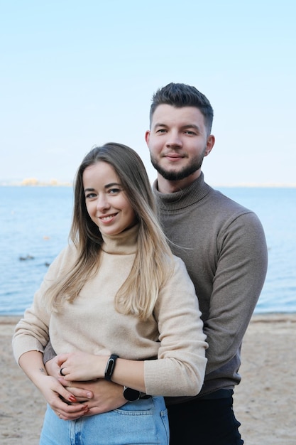 A bearded young man hugs a girl from behind Couple smiling and looking at the camera