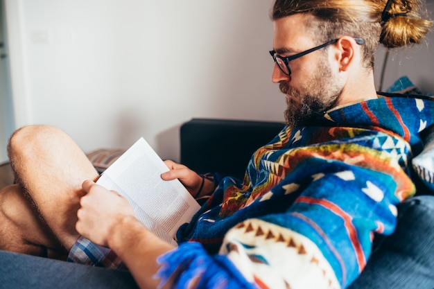 Bearded young man reading book sitting couch at home