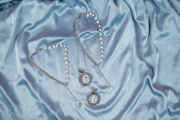 Beatiful stylish jewelry on silk draped fabric Chain necklace and earrings with pearls Blue satin background