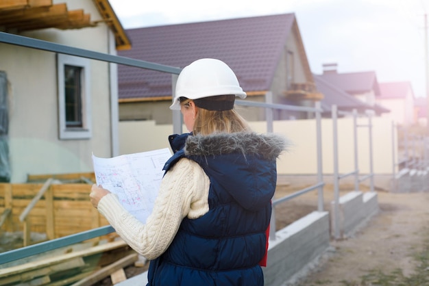 Beatiful woman engineer is standing serious in front of a building site