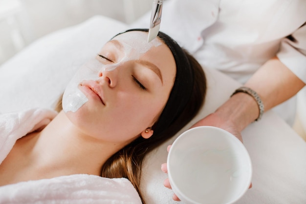 Beautican makes a mask to young woman in SPA salon. Closeup