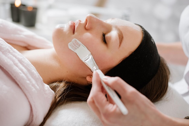 Beautican makes a mask to young woman in SPA salon. Closeup