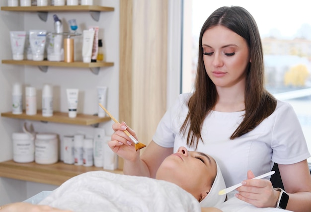 Beautician applies cosmetic product to patient woman with brush