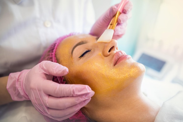 Beautician applies a golden mask to a woman's face