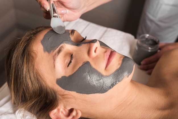 Beautician applying face mask on young woman's face