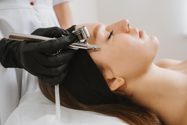 Beautician doing oxygen therapy for young woman laying down with closed eyes in a beauty salon