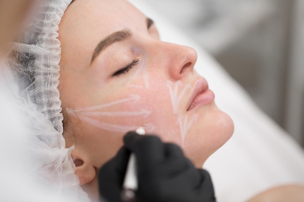 Beautician draws the contours of a white pencil on the face of the patient