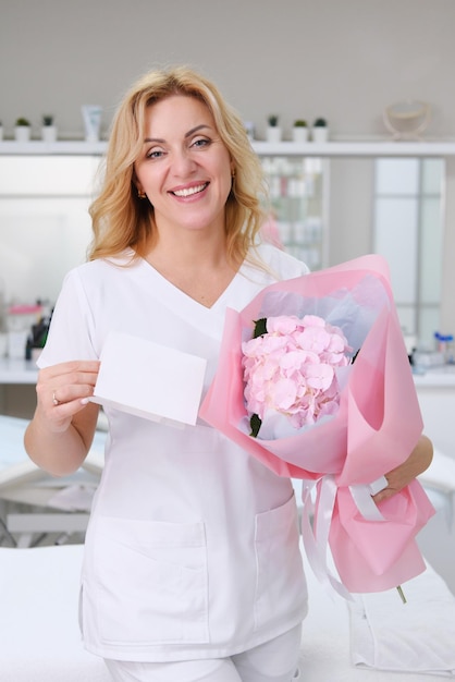 Beautician esthetician holds in his hands a bouquet of flowers and an empty form for a gift certificate Beauty treatment gift concept