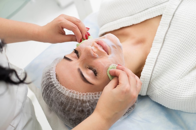 Beautician makes cleansing and exfoliating facial for beautiful girl. Beauty salon.