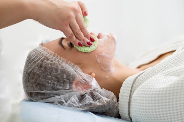 Beautician makes cleansing and exfoliating facial for beautiful girl. Beauty salon.