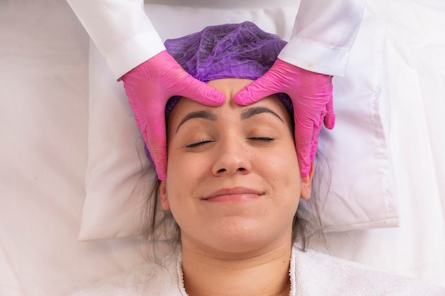 Photo beautician makes a professional massage of the face of the neck and shoulders for a young girl in the spa salon the view from the top facial beauty treatment