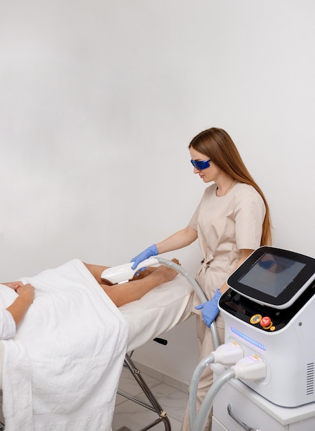 Beautician making hair removing procedure on legs for woman client Laser epilation and cosmetology in beauty salon