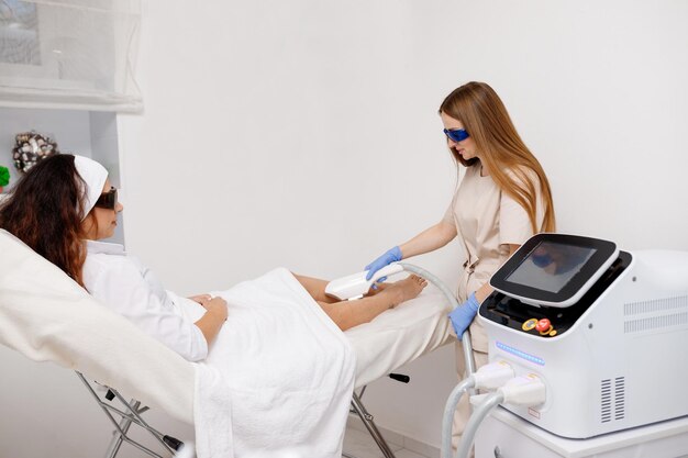 Beautician making hair removing procedure on legs for woman client Laser epilation and cosmetology in beauty salon