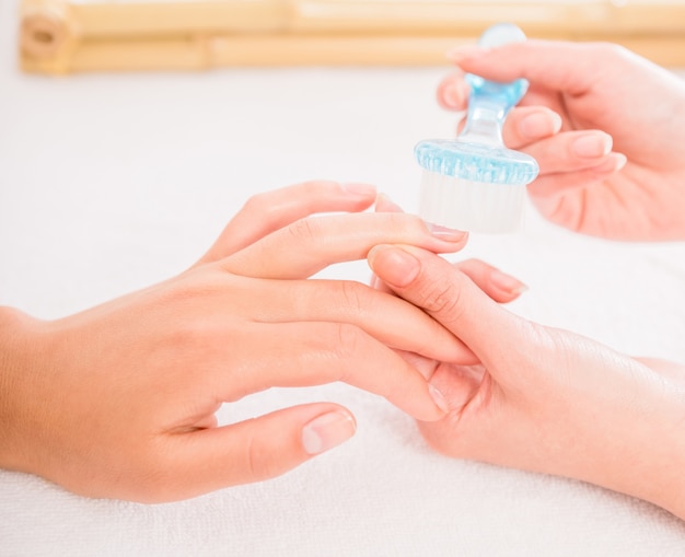 Beautician nails with brush to her client in beauty salon.