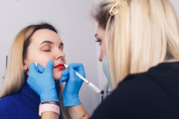 The beautician prepares the lips for permanent makeup the model looks in the mirror