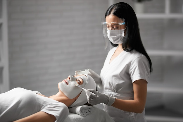 Beautician in protective mask doing peeling for patient