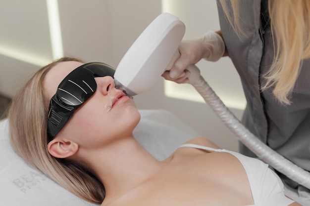 Beautician removes hair on beautiful female face using a laser hair removal in beauty clinic