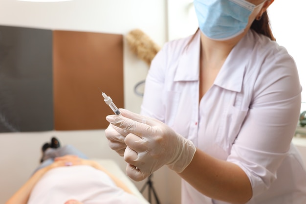 A beautician wearing sterile white gloves holds a hyaluronic acid injection filler and looks at it