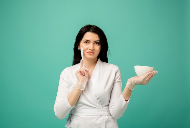 Beautician in a white uniform stands with a spatula and a cup on blue