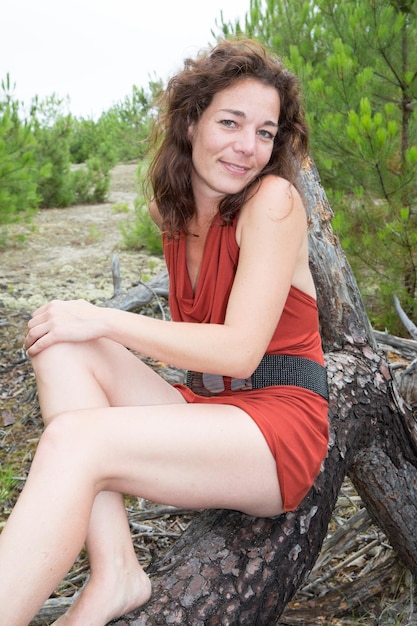 Beautiful 40 year old brunette woman middle aged sit on tree branch on sea beach coast