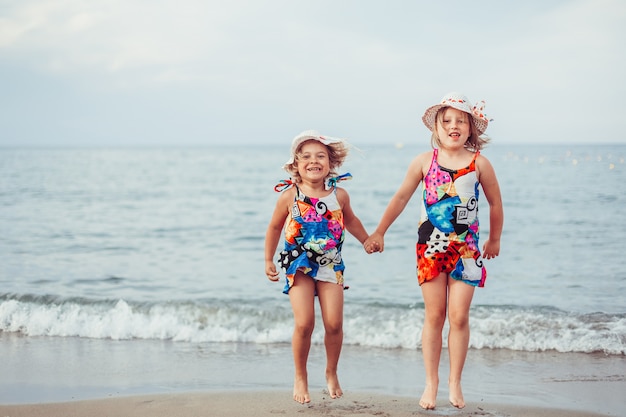 Beautiful adorable little girls together casual female portrait lifestyle beauty joyful girls holding hands on sea beach play. Childhood concept