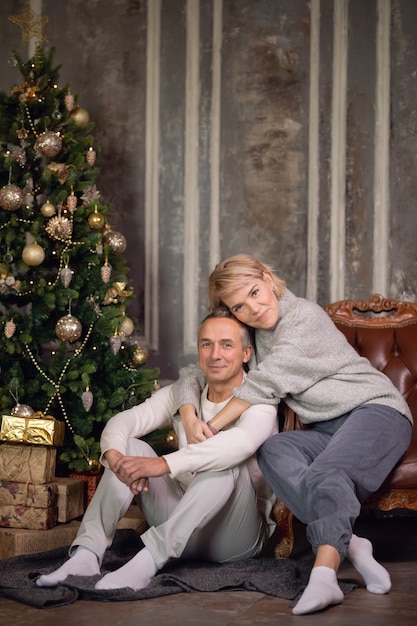 beautiful adult woman with a man sit on an armchair and hug near a christmas tree