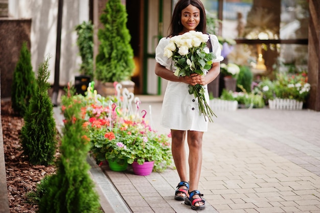 Beautiful african american girl holding bouquet of white roses flowers on dating in the city Black businesswoman with bunch of flowers