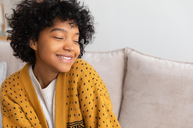 Beautiful african american girl with afro hairstyle smiling sitting on sofa at home indoor young afr