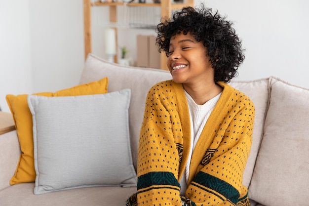 Beautiful african american girl with afro hairstyle smiling sitting on sofa at home indoor young afr